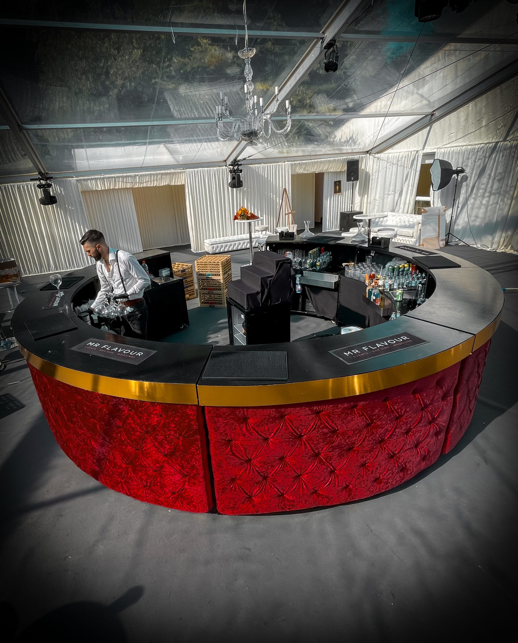 Circular mobile bar hire setup with red Chesterfield panels, full bar equipment, and professional bartender by Mr Flavour.