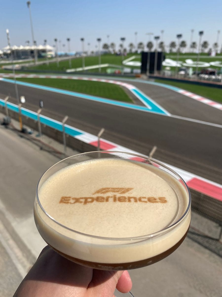 Branded espresso martini finished on a Ripples drink printer, carrying the F1 mark on the crema, held against the Yas Marina Circuit straight
