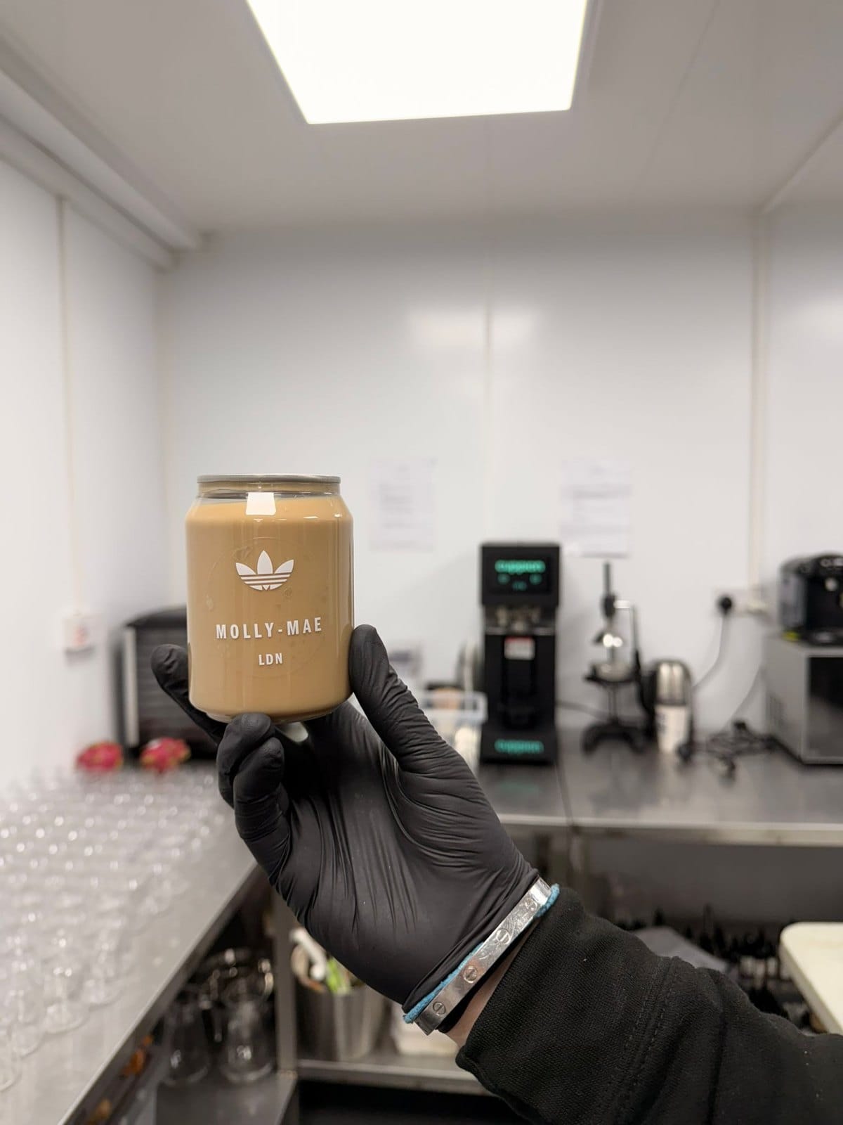 Gloved hand holding a finished Molly-Mae LDN iced latte can inside the five-star hygiene-rated production kitchen