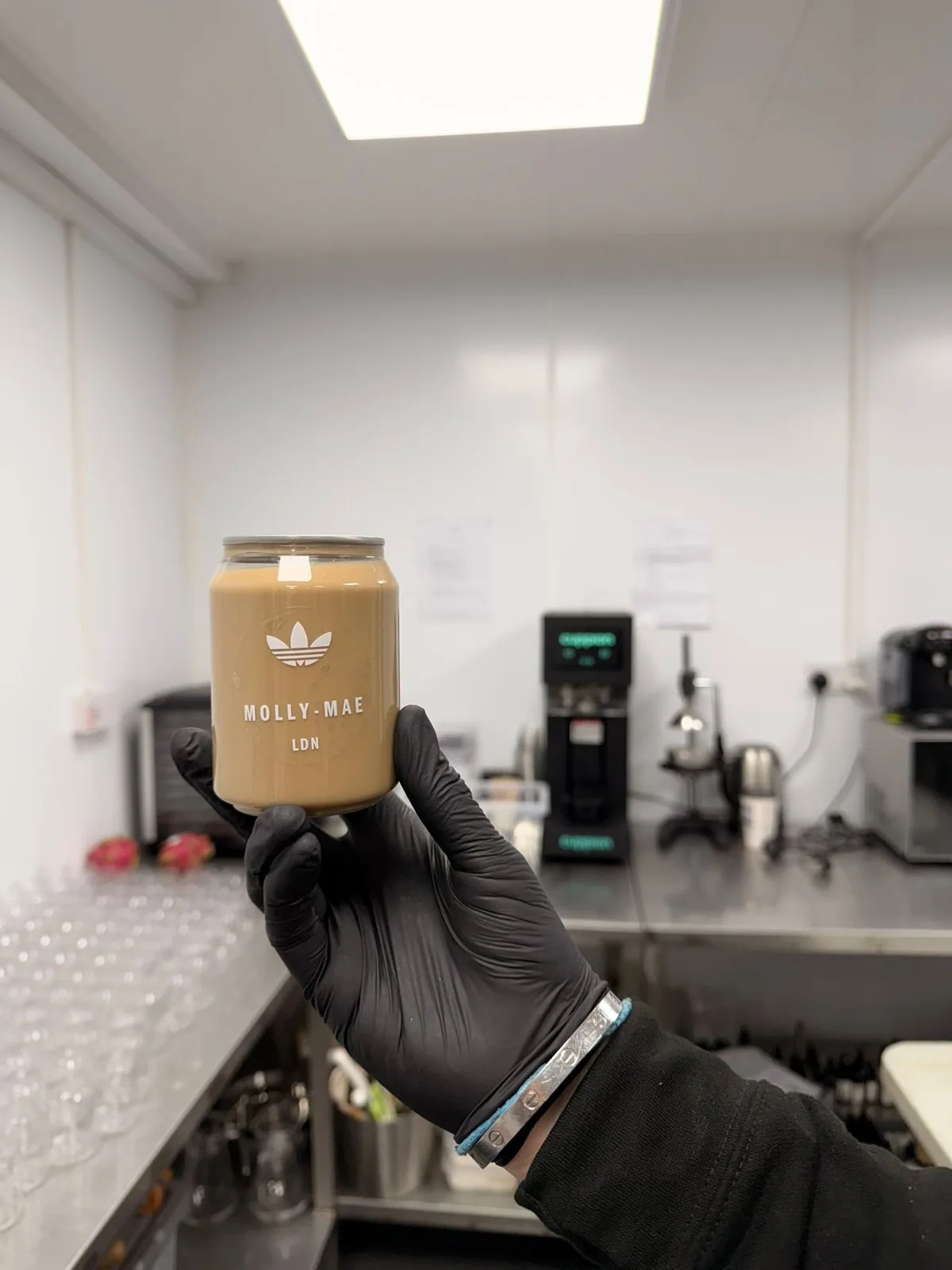 Gloved hand holding a finished Molly-Mae LDN iced latte can inside the five-star hygiene-rated production kitchen