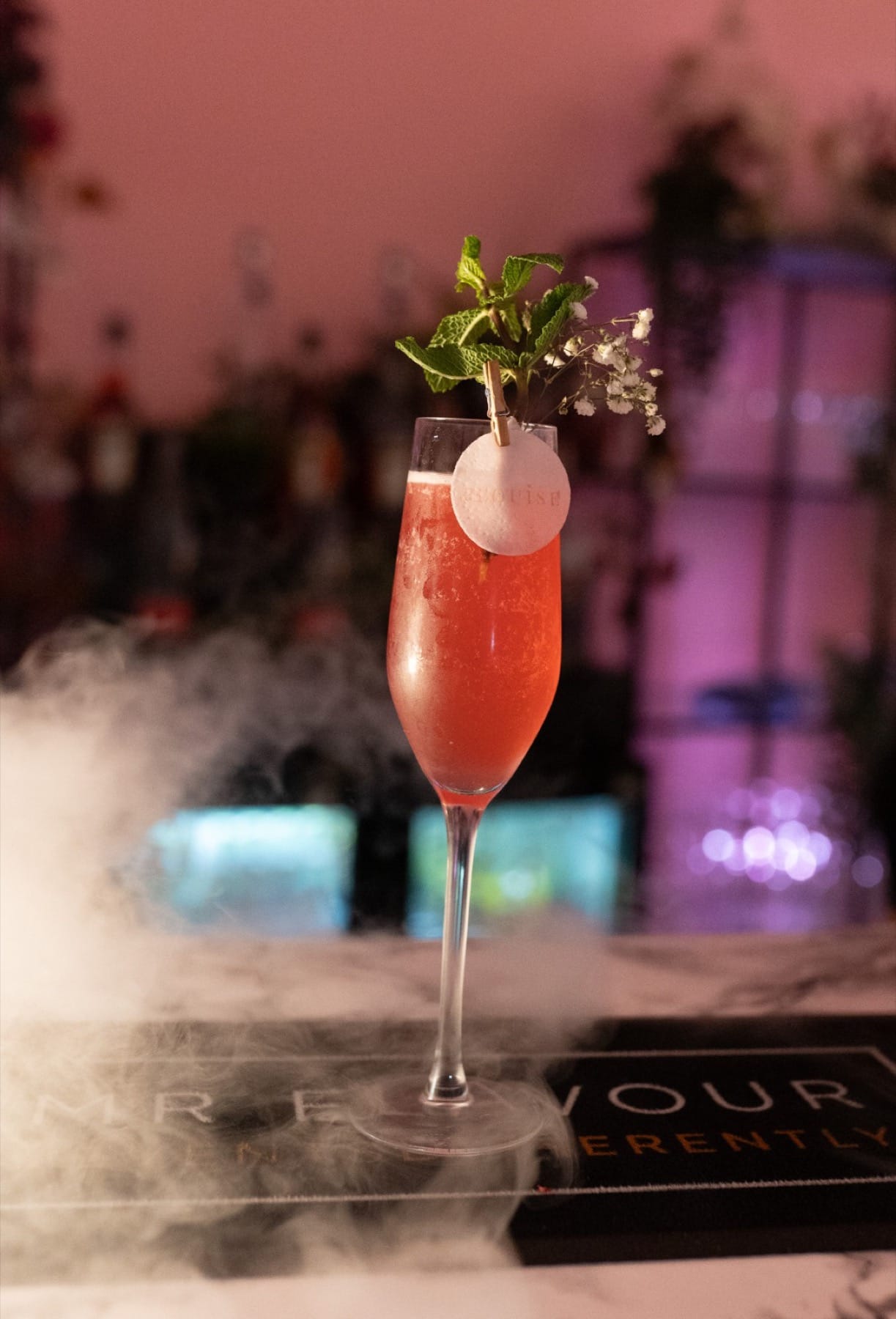Pink P.Louise branded cocktail with dry ice and floral garnish