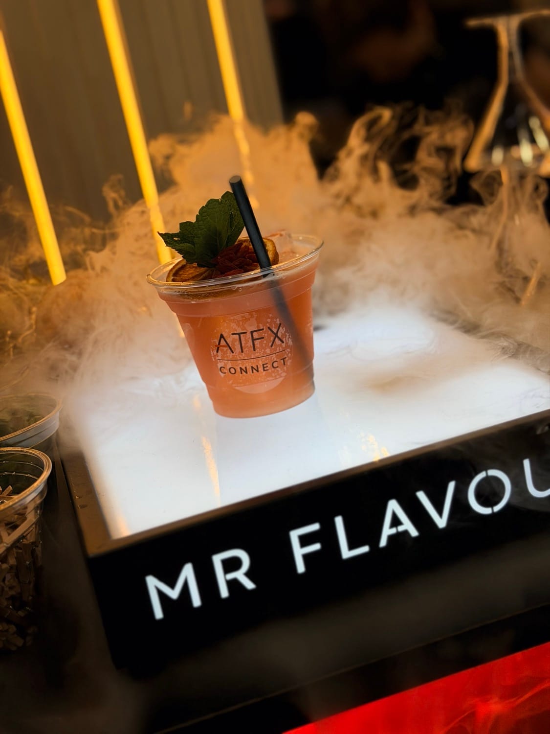 A branded ATFX signature serve finished with dry ice on the illuminated Mr Flavour counter at the Finance Magnates London Summit