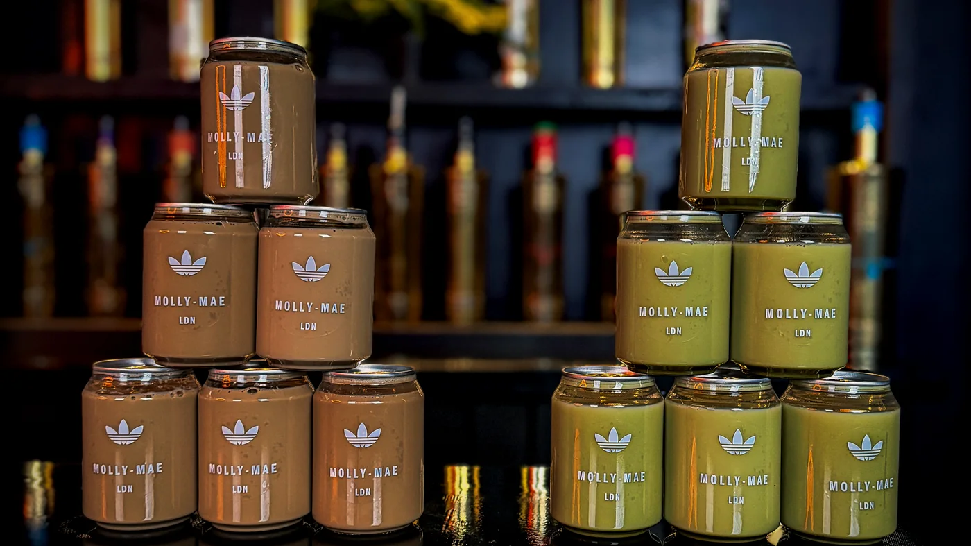 Two stacked pyramids of clear Mr Flavour cans on a bar, one iced latte and one matcha, wrapped in Molly-Mae LDN and adidas artwork.