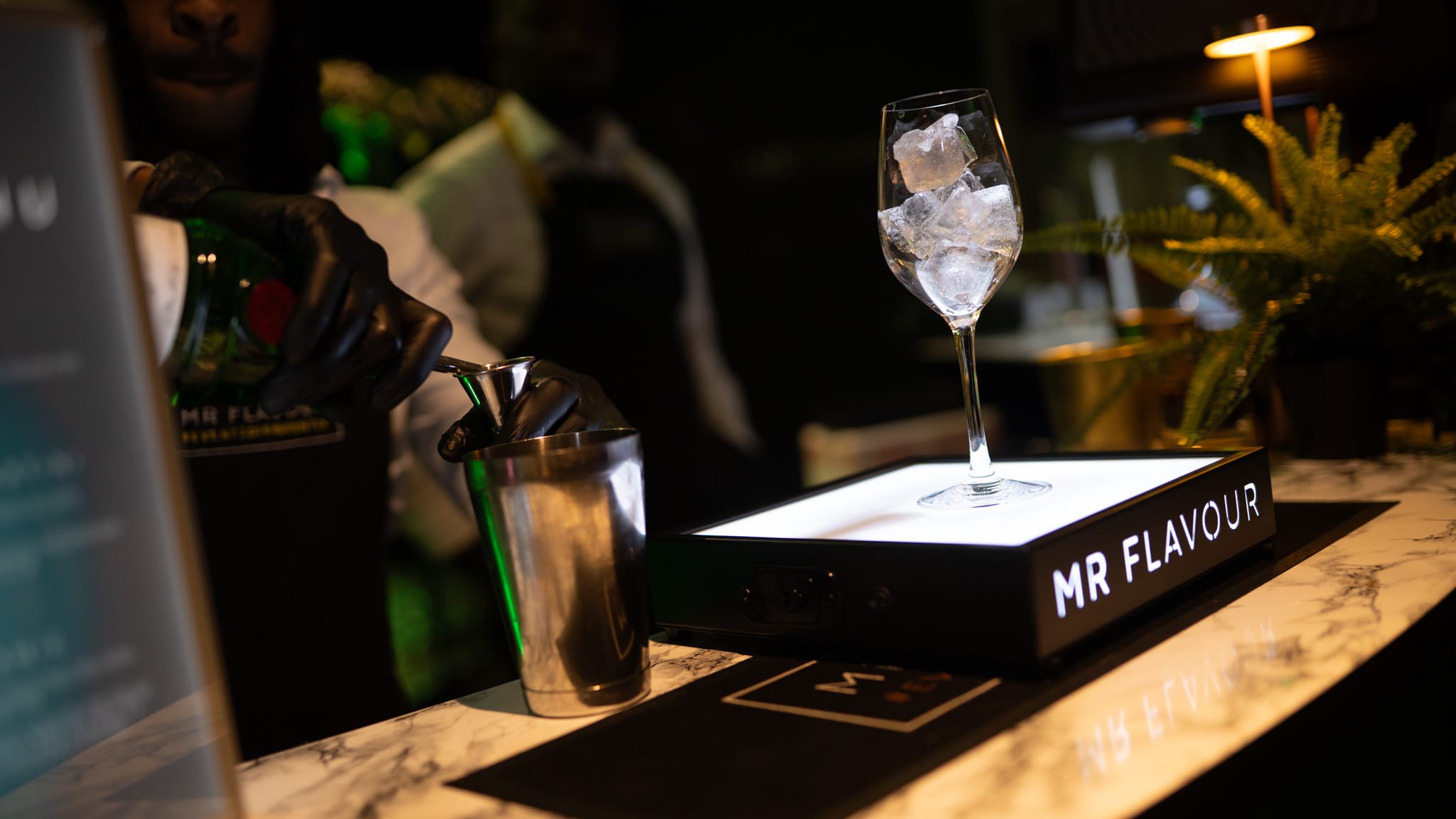Mixologist pouring a signature cocktail at a marble bar with a Mr Flavour branded lightbox during a luxury cocktail bar hire
