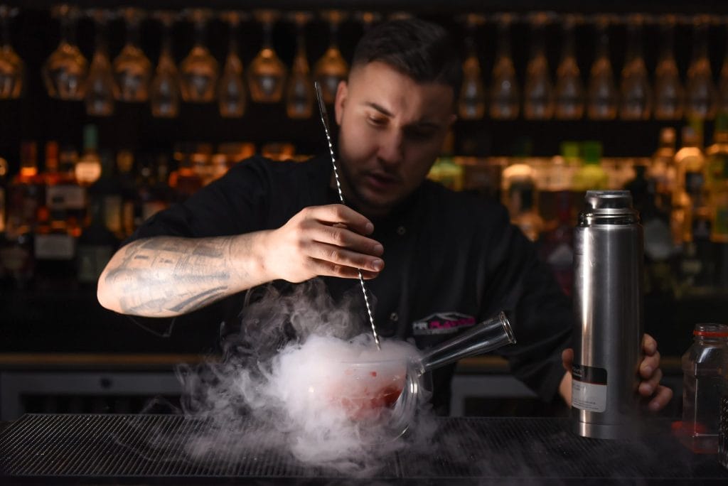 Mr Flavour bartender stirring a liquid nitrogen cocktail in a cloud of vapour at a back bar